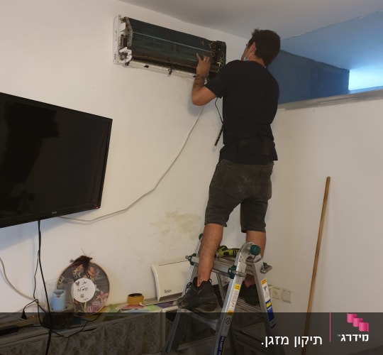 אדם מתקן מזגן על סולם בחדר